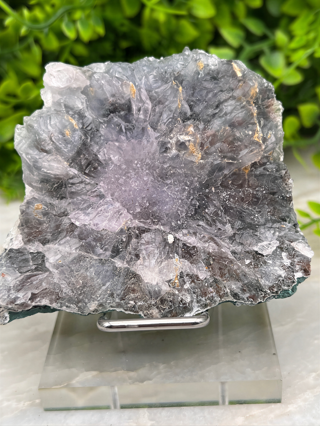 a large, irregularly shaped crystal formation with a mix of gray and white colors, placed on a glass stand.