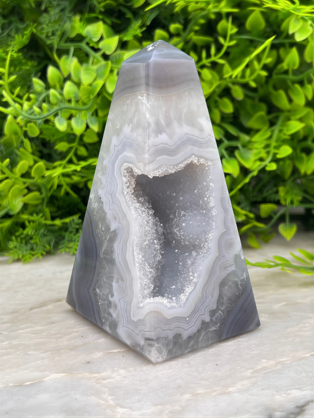 A triangular, geode-like rock formation with a large, open, and cracked surface, surrounded by lush green foliage.