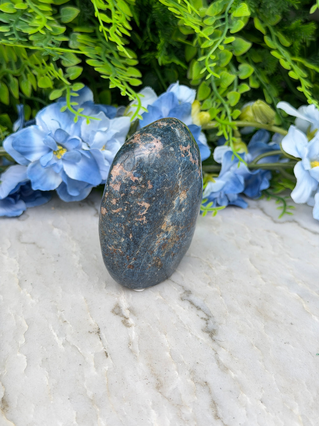 A dark gray rock rests on a white surface, surrounded by vibrant blue flowers.
