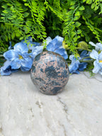 A close-up image of a speckled stone or gemstone resting on a white surface, surrounded by vibrant blue flowers.