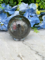 A close-up image of a gray crystal ball surrounded by blue flowers, with a white marble surface in the background.