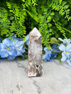 a close-up view of a stone or crystal object surrounded by lush green foliage and blue flowers.