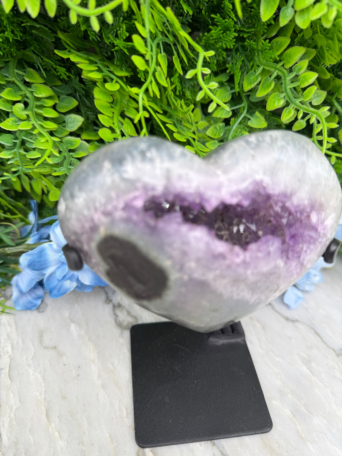 a purple amethyst crystal surrounded by green foliage and blue flowers.