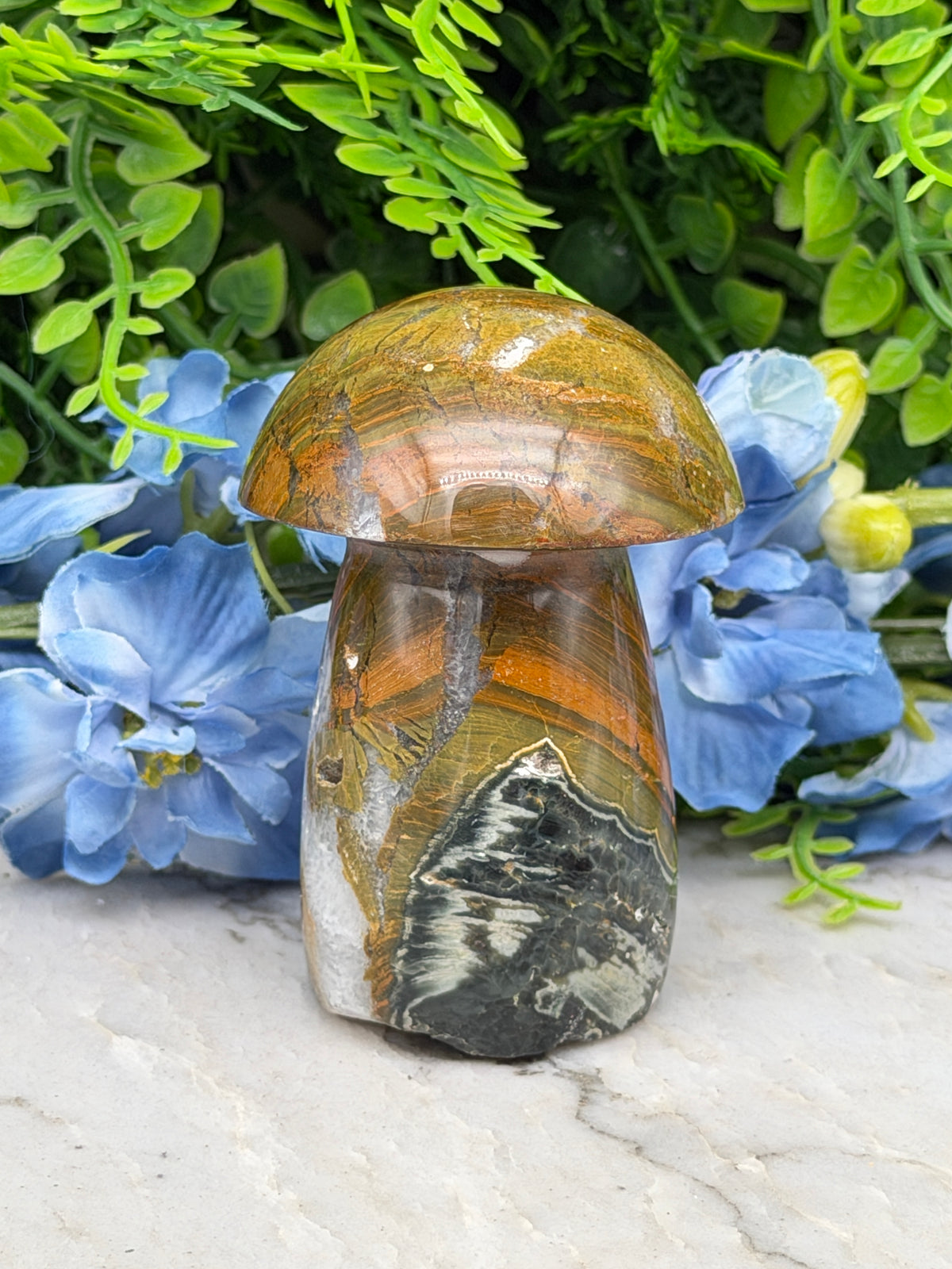 a close-up view of a natural stone mushroom-shaped object, surrounded by vibrant blue flowers.