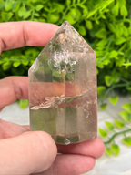 A hand is holding a clear crystal with a jagged edge, set against a blurred green background.