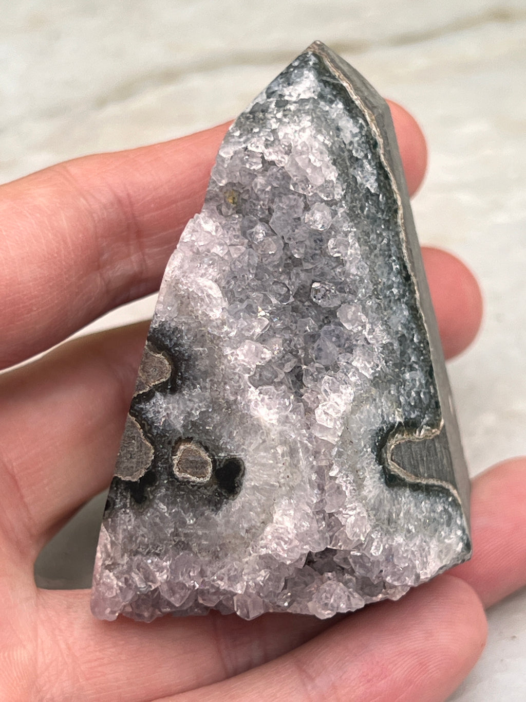 A hand is holding a piece of a crystal, which appears to be a piece of amethyst.