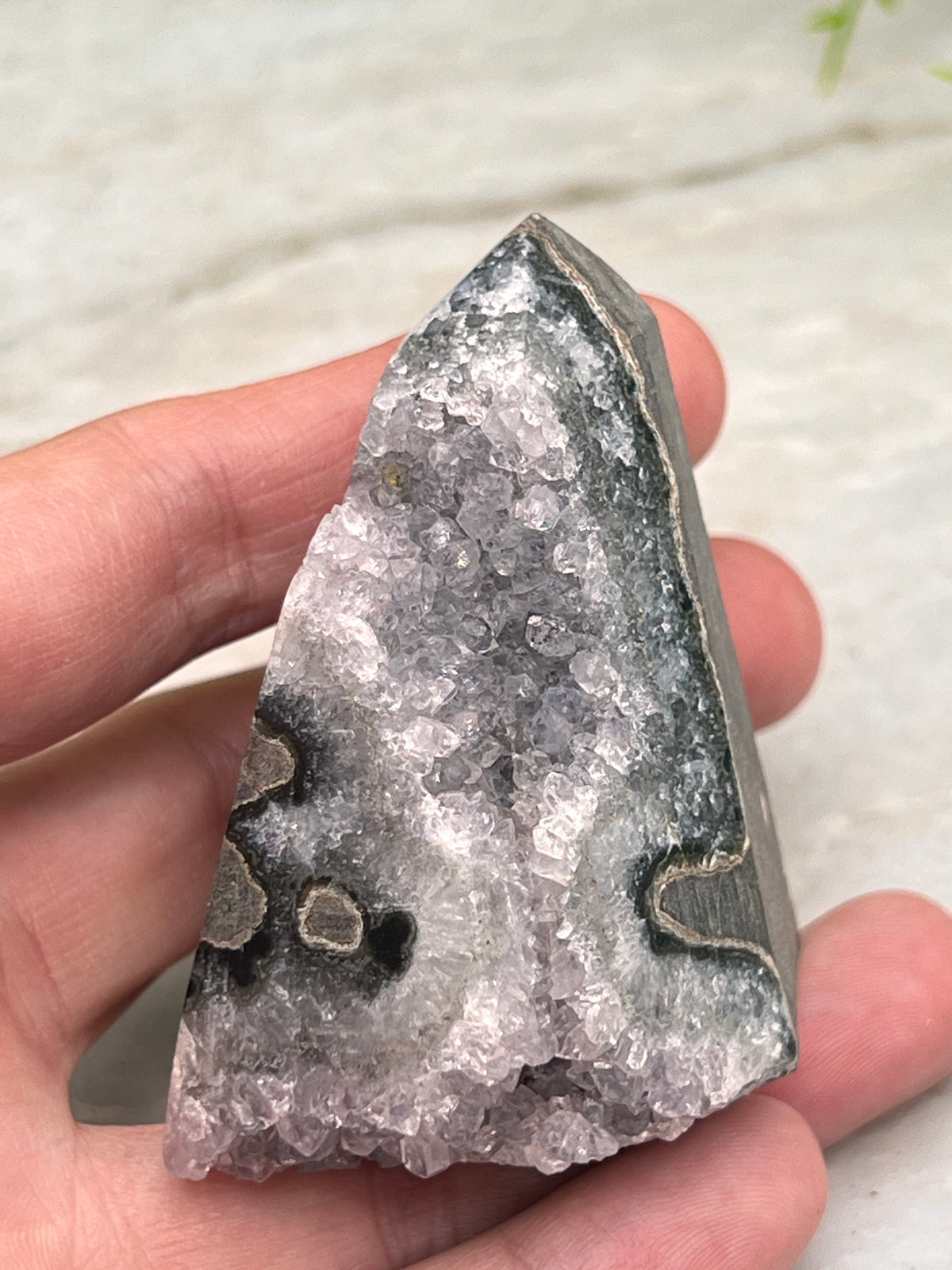 A hand is holding a piece of rock with a unique, jagged shape and a mix of gray and white crystals.