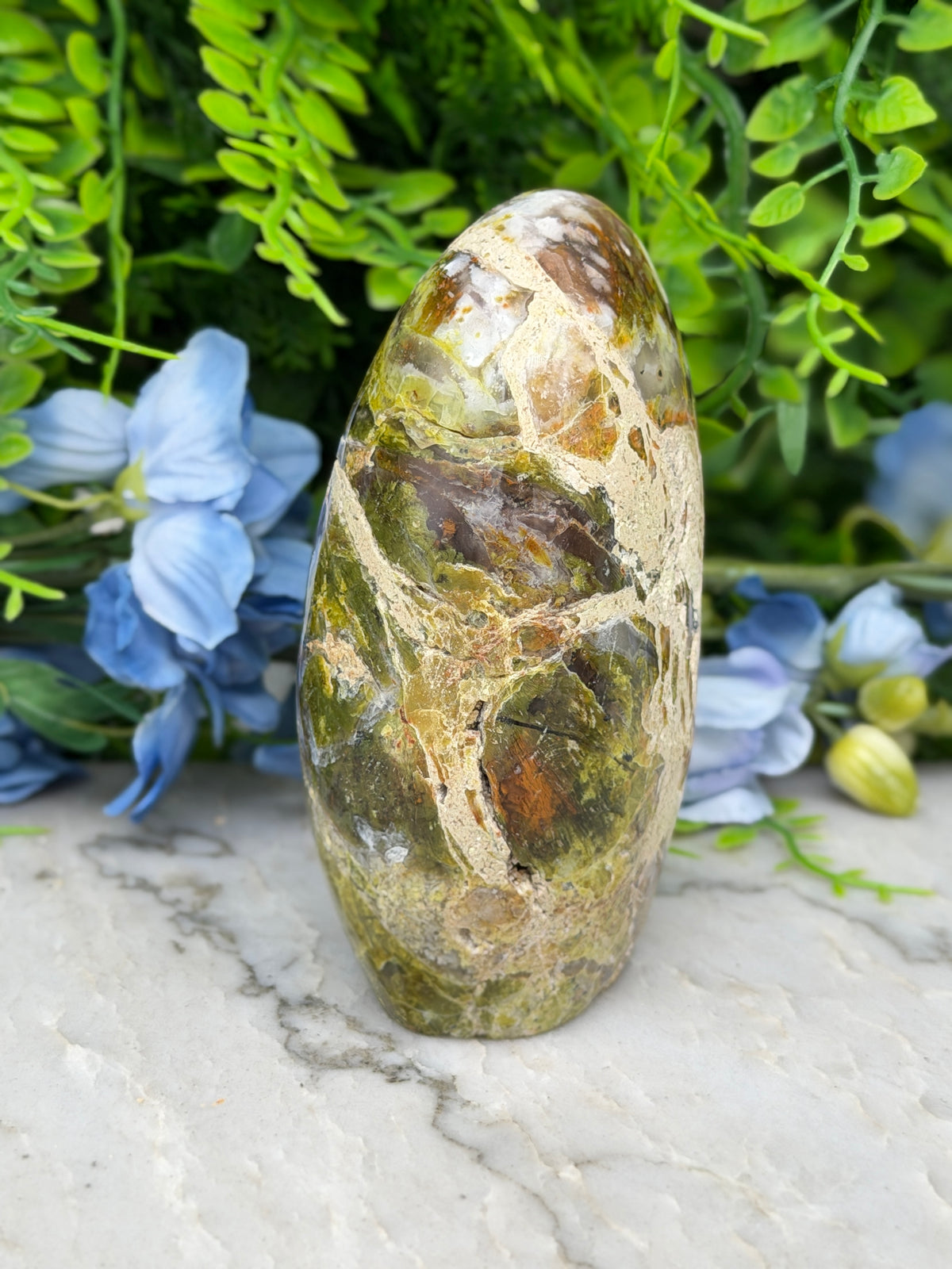 a natural stone with a unique, colorful pattern, surrounded by lush greenery and blue flowers.