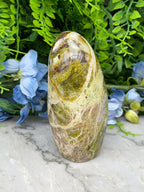 a natural stone with a unique, textured surface, surrounded by lush greenery and vibrant blue flowers.