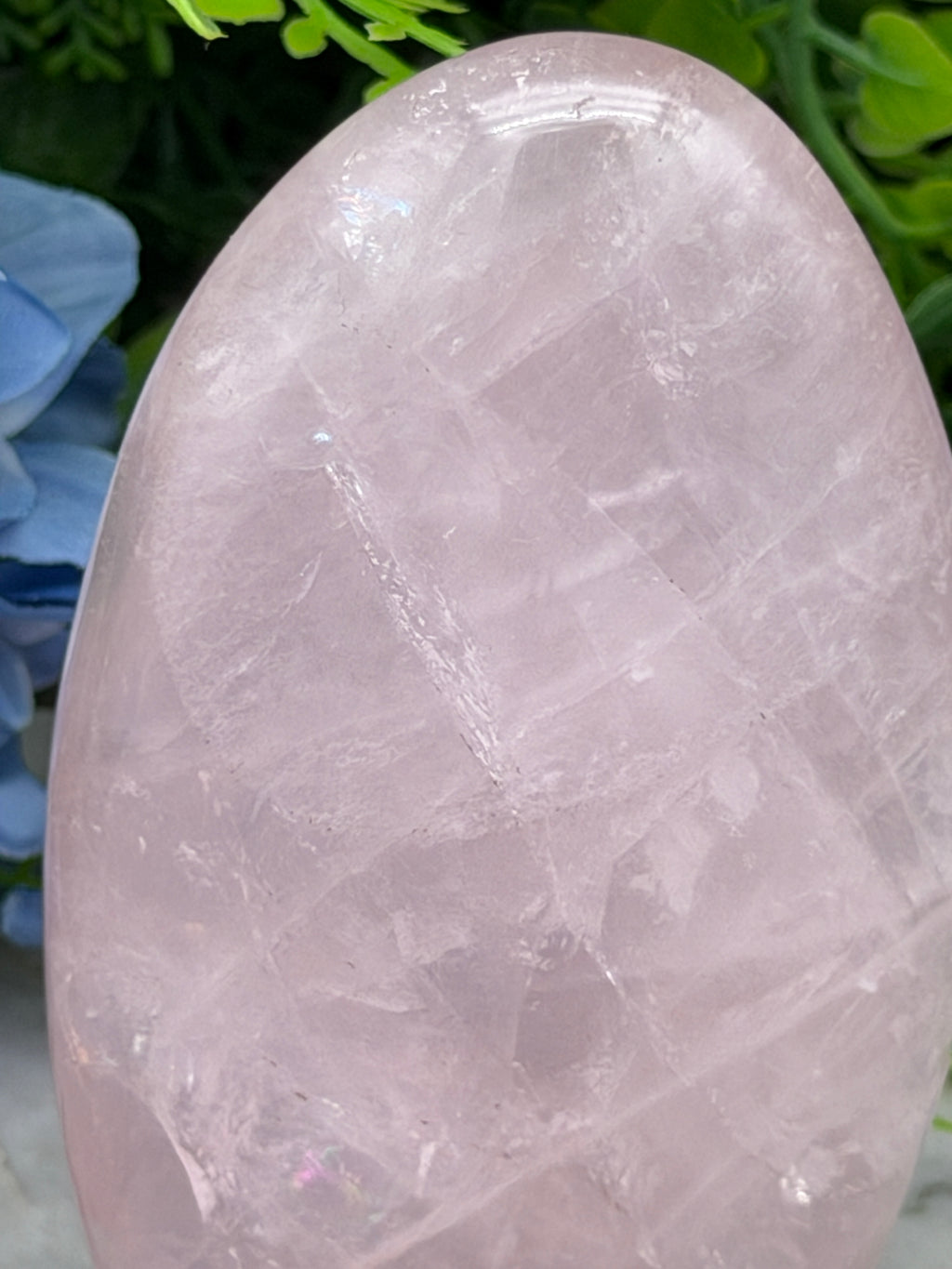 A close-up image of a pink crystal or gemstone, with a blurred background of green foliage.