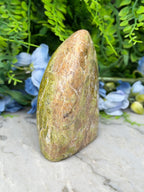a natural stone with a unique, irregular shape, surrounded by lush green foliage and blue flowers.
