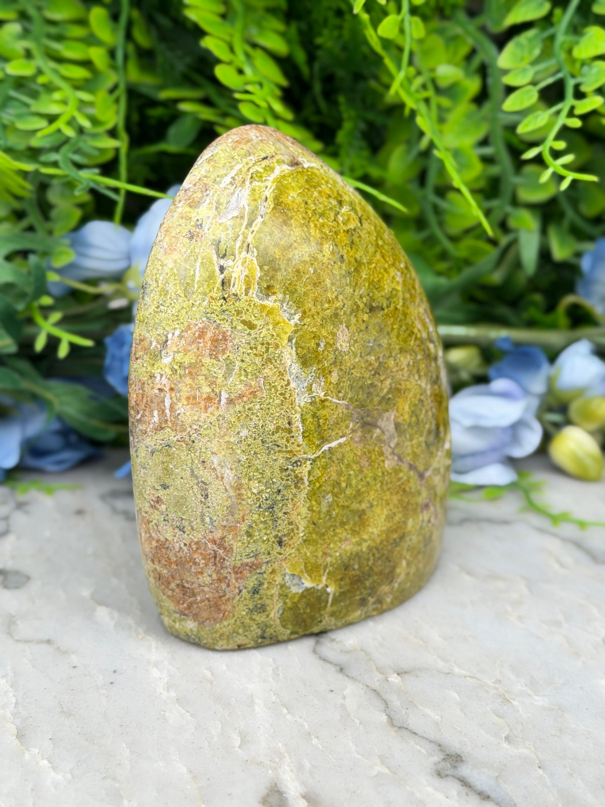 a large, jagged, and textured rock formation with a greenish hue, set against a backdrop of lush, green foliage.