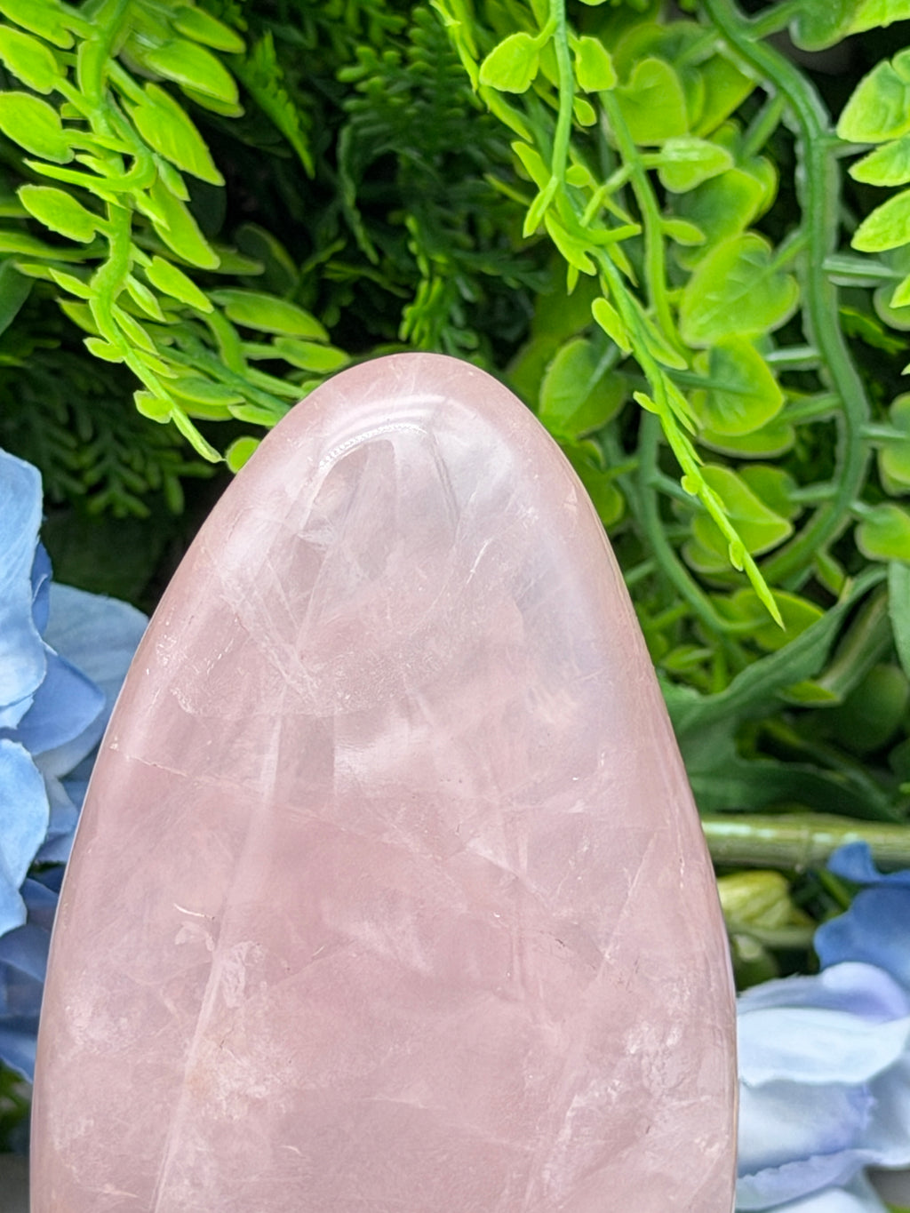 A close-up image of a pink gemstone, possibly a piece of jade, set against a background of green foliage.
