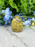 a yellowish-brown stone, possibly a gemstone, placed on a marble surface surrounded by blue flowers and greenery.