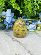 a yellowish-brown stone, possibly a gemstone, placed on a marble surface surrounded by blue flowers and greenery.