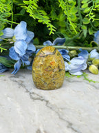 a yellowish-brown stone or rock sitting on a marble surface, surrounded by blue flowers and green foliage.
