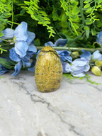 a yellowish-brown stone or rock placed on a marble surface, surrounded by blue flowers and green foliage.