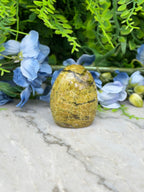 a yellowish-brown stone or rock placed on a marble surface, surrounded by blue flowers and green foliage.