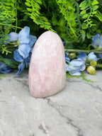 A pink crystal rests on a marble surface, surrounded by blue flowers and greenery.