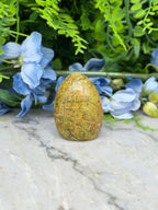 a yellowish-brown stone or rock placed on a marble surface, surrounded by blue flowers and greenery.
