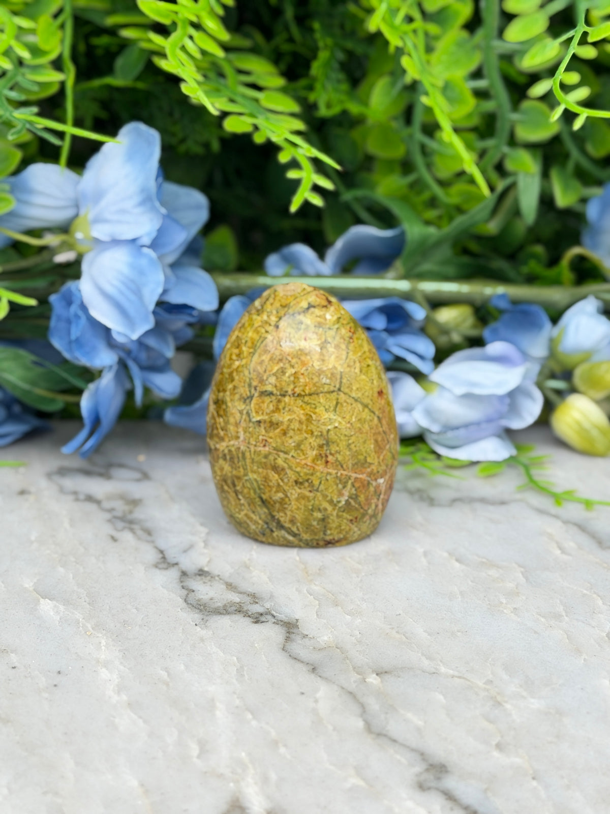 a yellowish-brown stone or rock placed on a marble surface, surrounded by blue flowers and greenery.