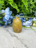 a yellowish-brown stone or rock placed on a marble surface, surrounded by blue flowers and green foliage.