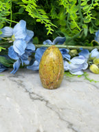 a yellowish-brown stone or gemstone placed on a marble surface, surrounded by blue flowers and greenery.