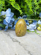 a yellowish-brown stone, possibly a jade or amber, surrounded by blue flowers and green foliage.