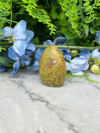 a yellowish-brown stone or rock placed on a marble surface, surrounded by blue flowers and green foliage.
