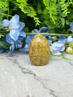 a yellowish-brown stone or gemstone placed on a marble surface, surrounded by blue flowers and greenery.