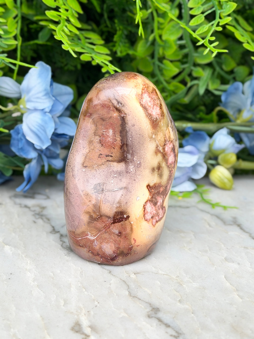 a large, brown, and speckled rock sitting on a marble surface, surrounded by blue flowers.
