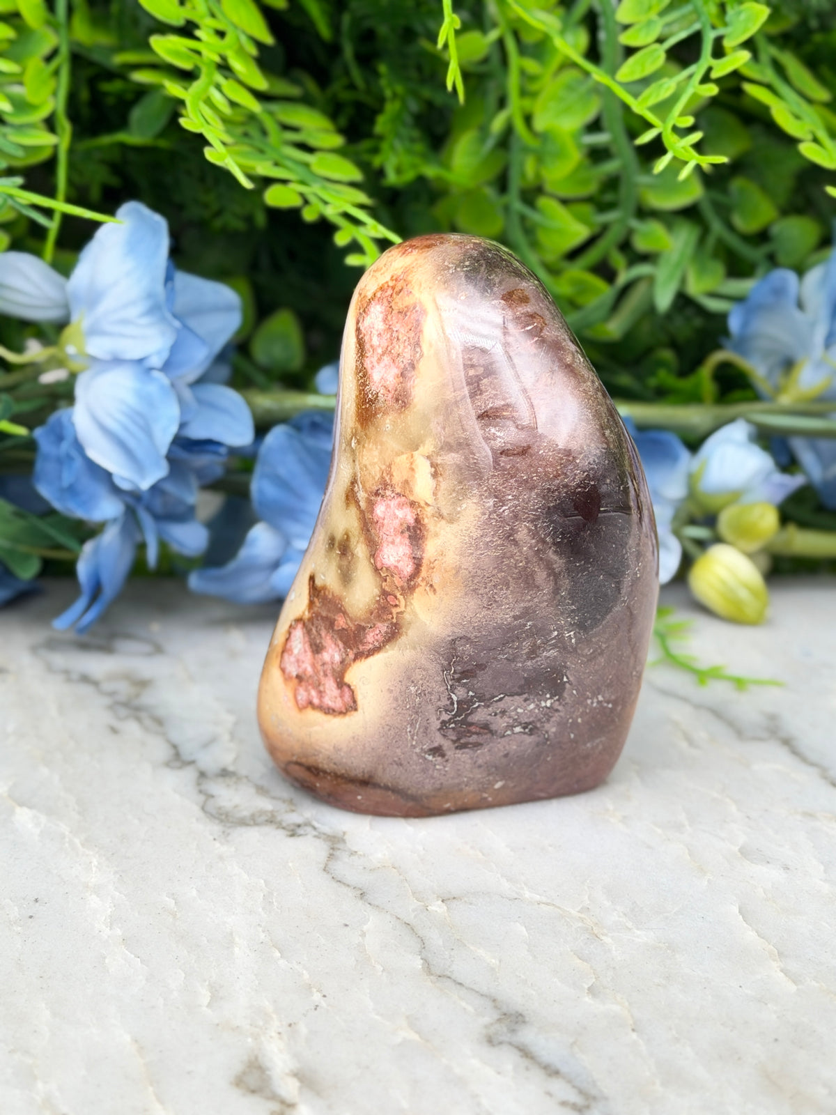 a brown, speckled rock sitting on a white marble surface, surrounded by blue flowers.