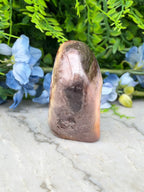 a brown, irregularly shaped rock with a dark, speckled surface, placed on a white marble surface. The rock is surrounded by blue flowers, creating a visually appealing contrast between the natural and the artificial elements.
