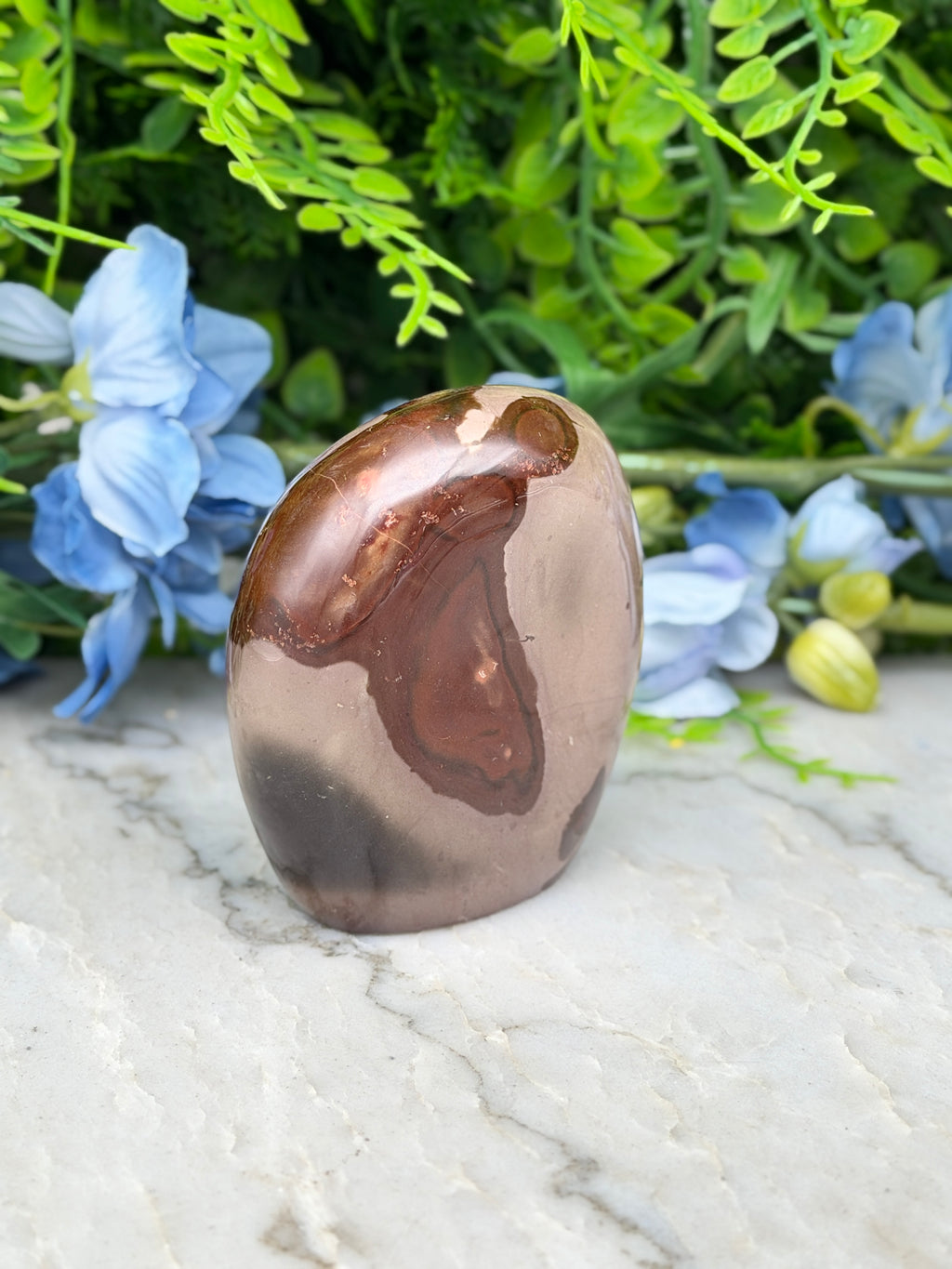 a brown and brown speckled rock sitting on a white marble surface, surrounded by blue flowers.