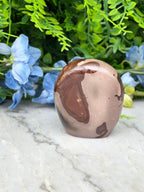 A brown, oval-shaped stone or gemstone is placed on a white marble surface, surrounded by blue flowers.