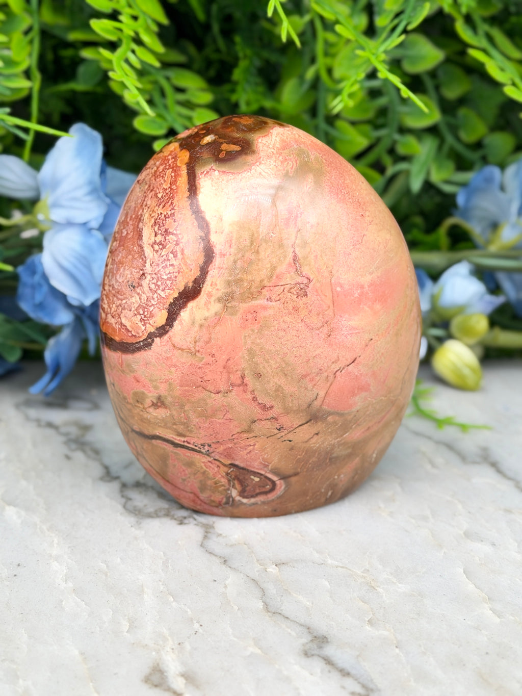 A pink and brown speckled rock sits on a marble surface, surrounded by blue flowers.