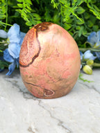 A pink and brown speckled rock sits on a marble surface, surrounded by blue flowers.
