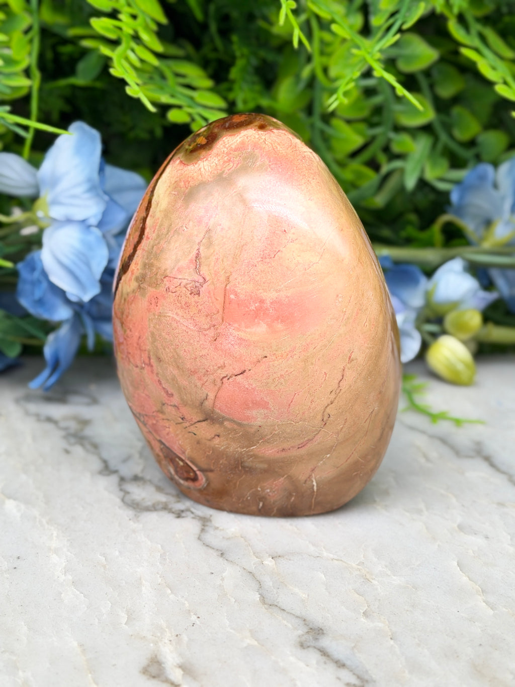 a pinkish-brown rock with a rough texture, placed on a white marble surface. The rock is surrounded by blue flowers, creating a visually appealing contrast.