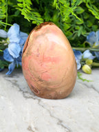 a pinkish-brown rock with a rough texture, placed on a white marble surface. The rock is surrounded by blue flowers, creating a visually appealing contrast.