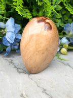 a wooden object with a brown and orange hue, placed on a marble surface. The object appears to be a piece of wood with a unique texture and pattern. The background is filled with lush green foliage, creating a natural and serene setting.