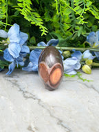 a brown, oval-shaped stone with a unique pattern, placed on a white marble surface. The stone is surrounded by blue flowers, creating a visually appealing contrast.