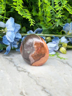 a brown and orange stone, possibly a jade or amber, placed on a white marble surface. The stone is surrounded by blue flowers and green foliage, creating a visually appealing and harmonious composition.