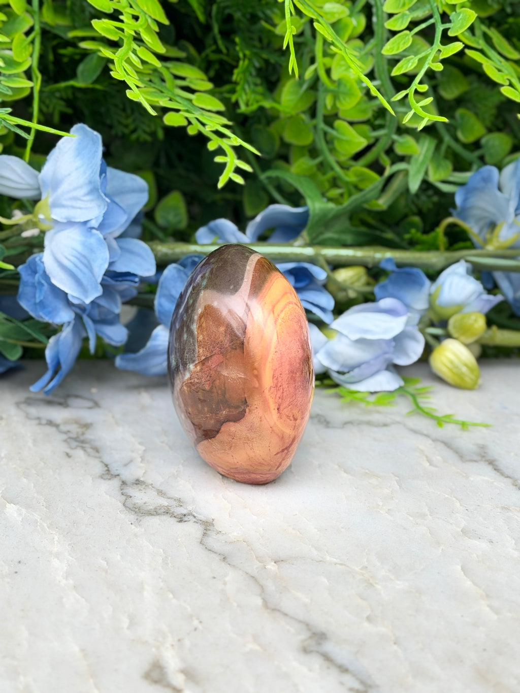 a brown and orange stone, possibly a jade or amber, placed on a marble surface surrounded by blue flowers.