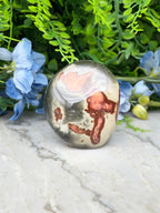 a jadeite gemstone with a unique, colorful pattern, surrounded by blue flowers and green foliage.
