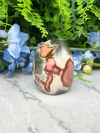 a jade egg, a natural stone with a unique, colorful pattern, placed on a marble surface surrounded by blue flowers.