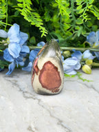 a pendant-shaped stone with a unique, colorful design, placed on a marble surface surrounded by blue flowers.