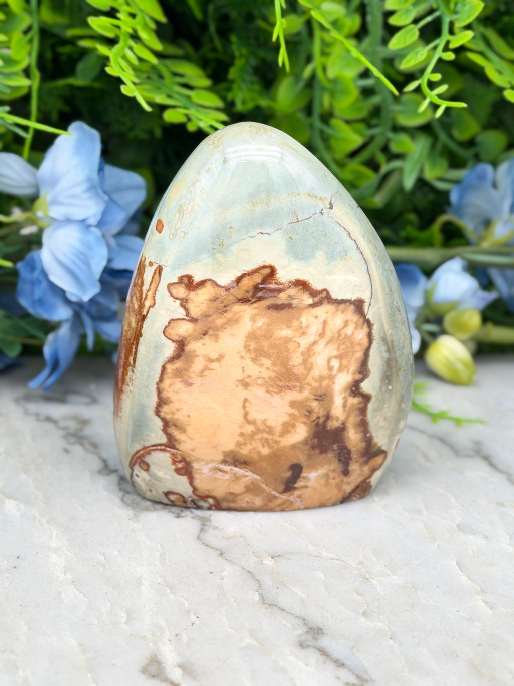 a light blue and brown speckled rock sitting on a white marble surface, surrounded by blue flowers.