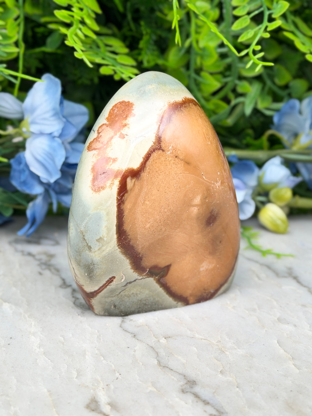 a large, colorful rock formation with a unique pattern, surrounded by lush green foliage and blue flowers.