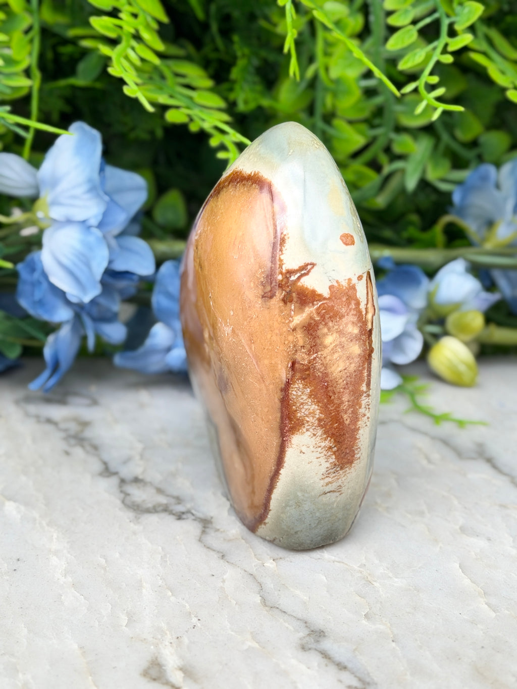 a stone with a unique, textured surface, surrounded by a variety of blue flowers and greenery.