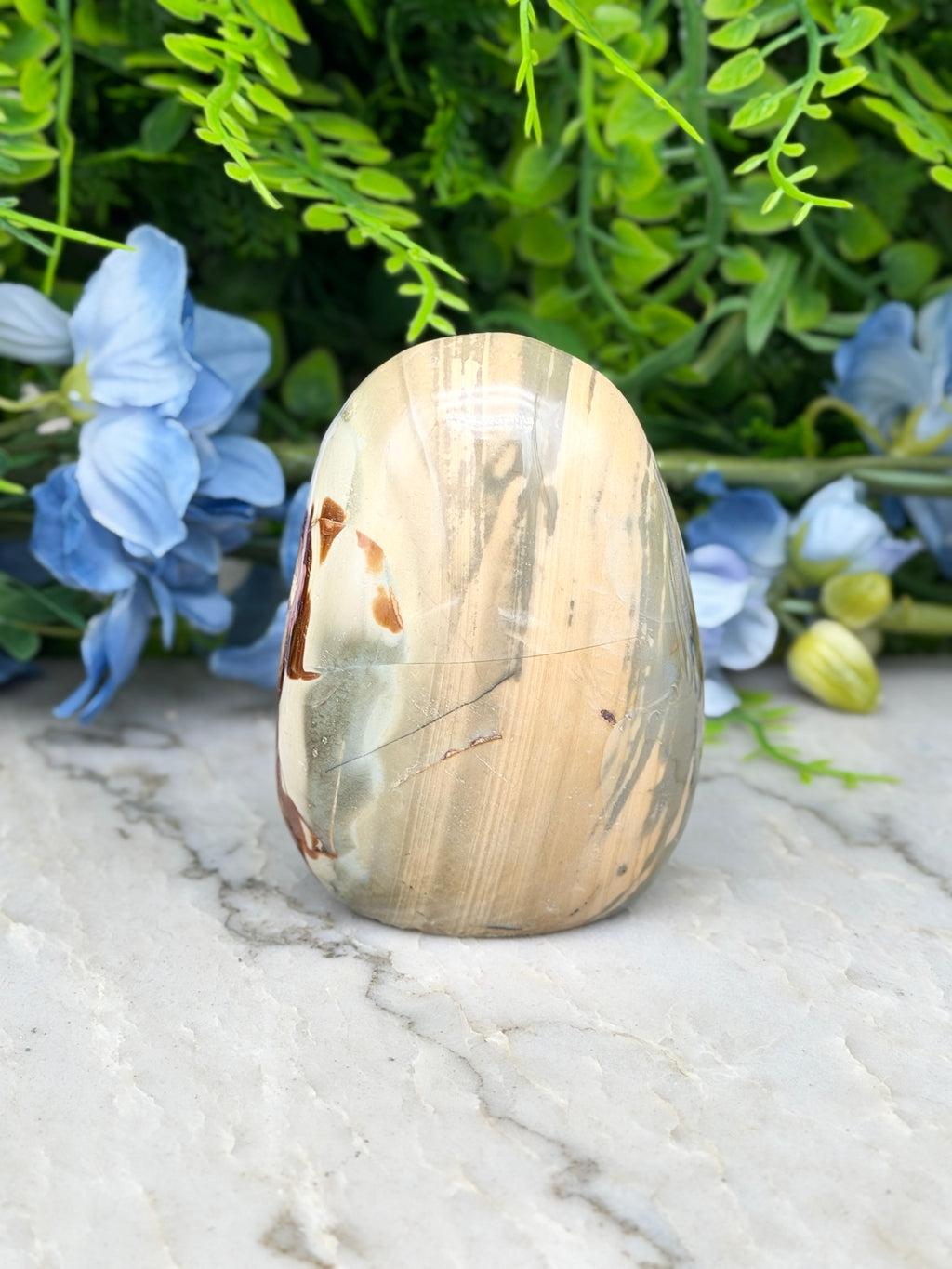 A natural stone, possibly a jade or slate, is displayed on a marble surface, surrounded by blue flowers.